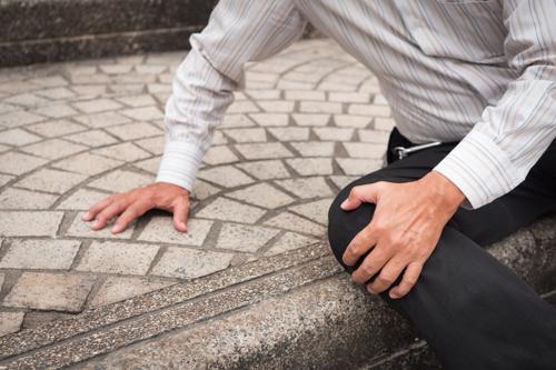 A man holding an injured knee after tripping on a staircase.