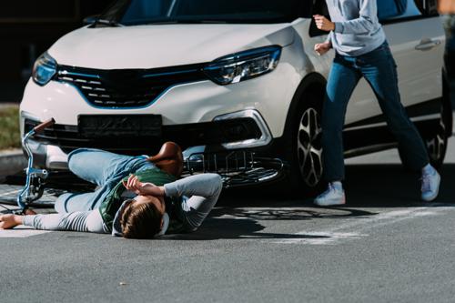 A man lying in the road after being hit by a car while on his bike.