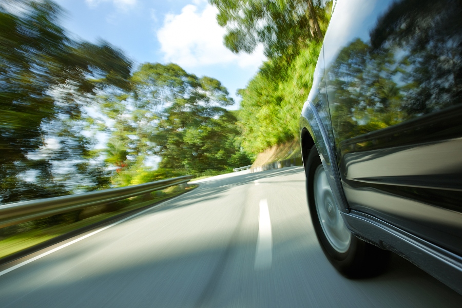 Black car speeding on tree-lined road