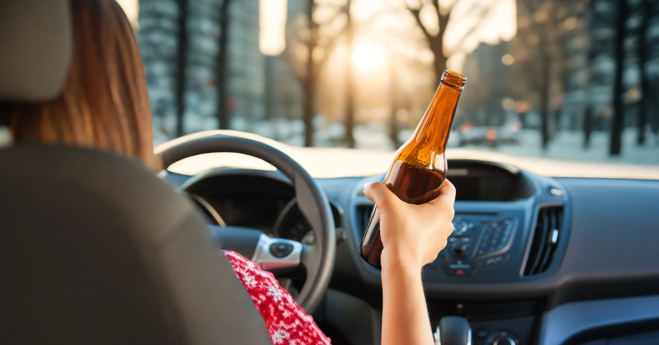 woman in holiday sweater driving while holding a beer