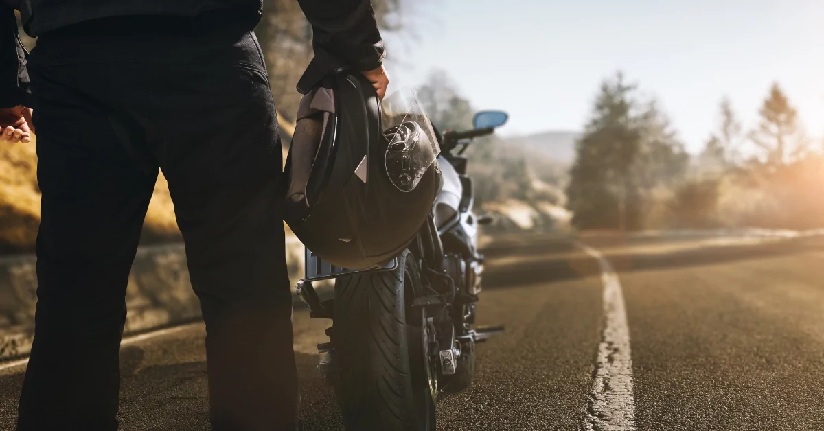Person holding a motorcycle helmet while standing near a motorcycle after an accident