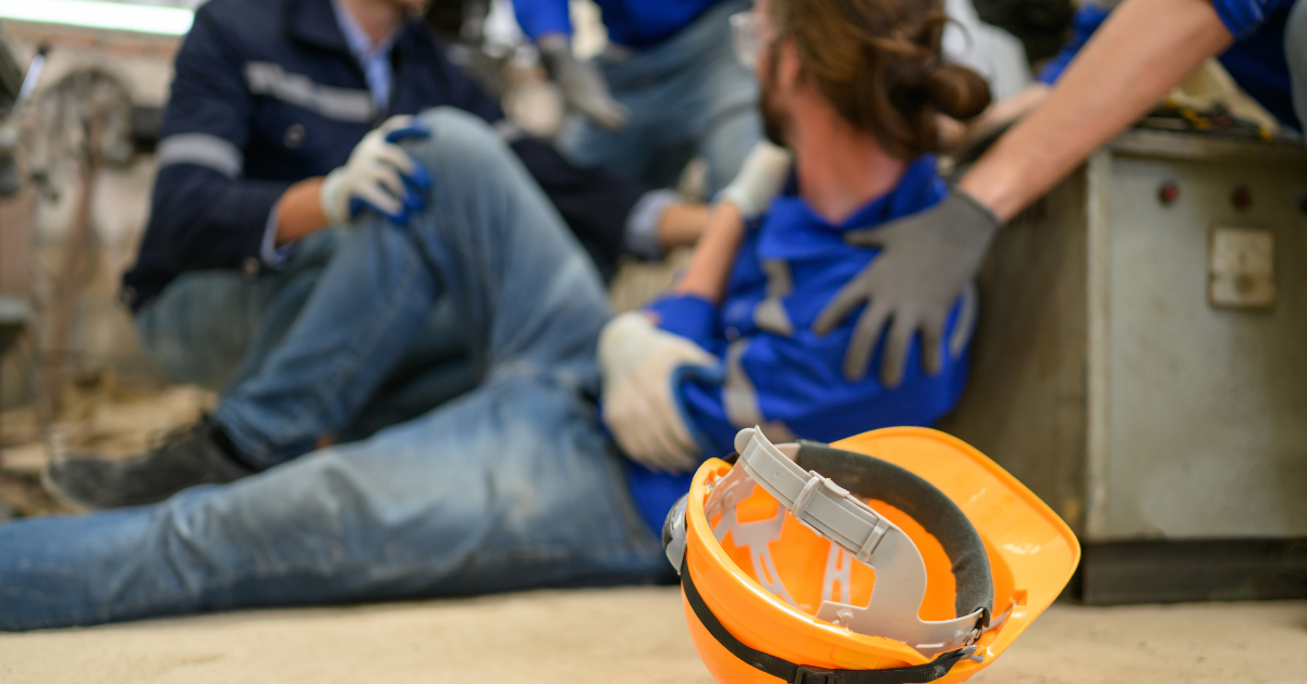 Injured construction worker holding his arm while coworkers help him at the jobsite.