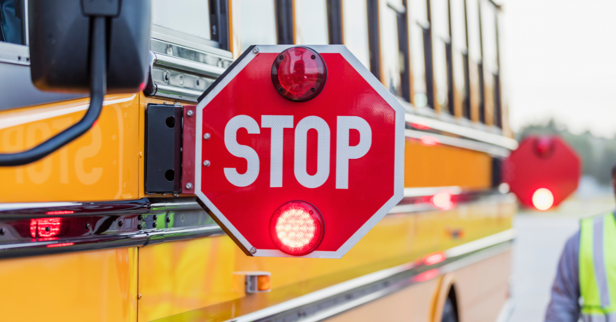 Close-up of a school bus stop sign with flashing red lights extended from the side of a yellow school bus.