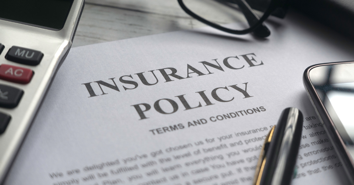Insurance policy document on a desk with a calculator, pen, glasses, and smartphone.