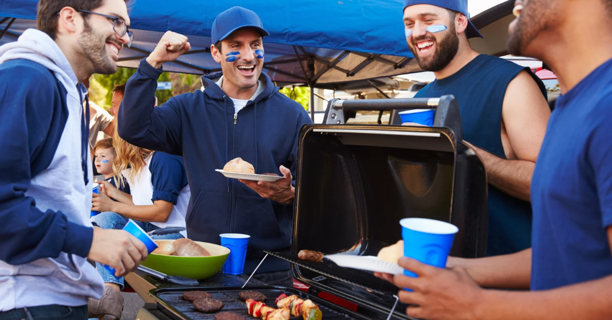 Group of sports fans at a tailgate in a parking lot outside of a stadium.