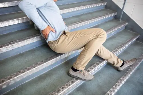 A man holding his lower back after slipping on a staircase.