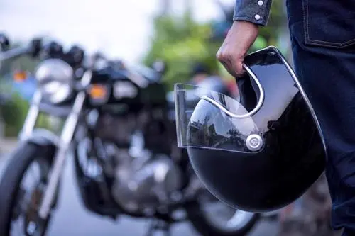 A man holding a helmet walking towards a motorcycle.