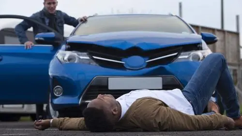 A man lying in the road after being hit by a car.