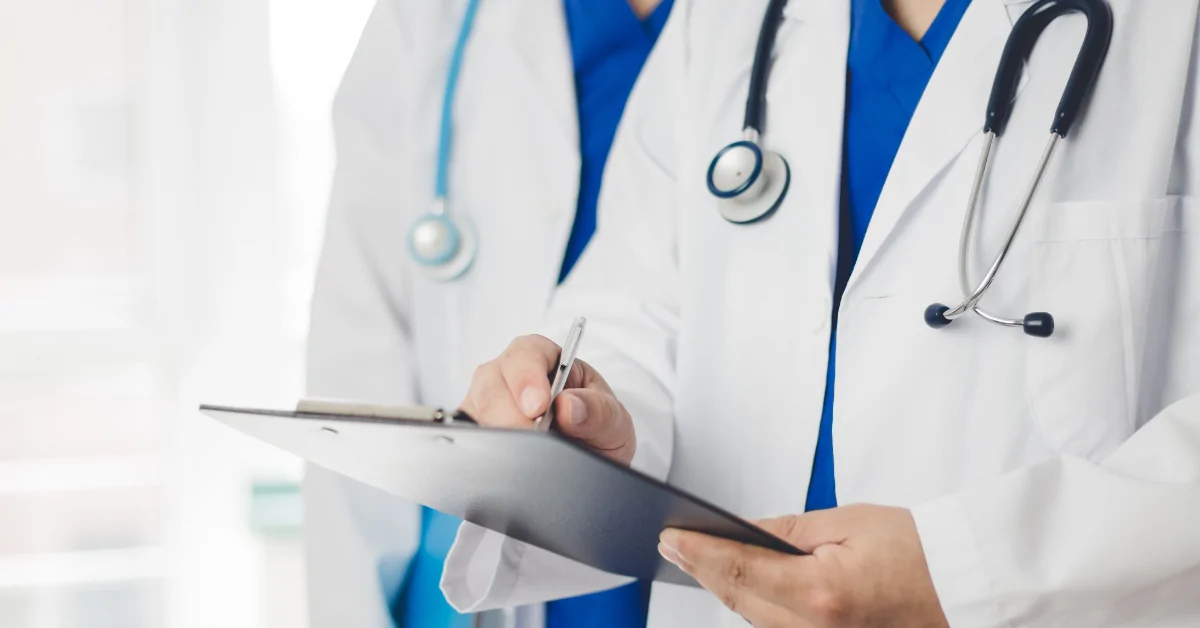 Healthcare professionals reviewing patient information on a clipboard while wearing white lab coats and stethoscopes.